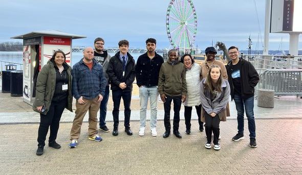 A group of students stand on a sidewalk in front of the National Harbor in Maryland. 